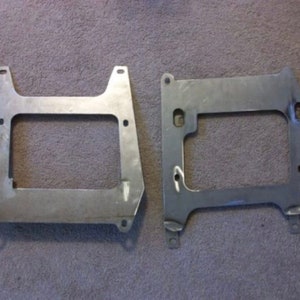 May include: Two metal brackets with rectangular cutouts. The brackets are made of a light gray metal and have a slightly textured surface.