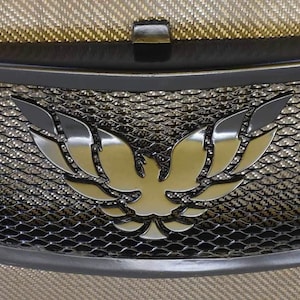 May include: Black metal grille with a silver phoenix emblem. The grille has a mesh design and is curved at the bottom.
