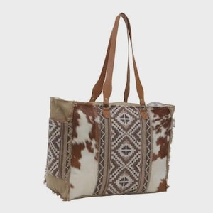 May include: A large tote bag with brown leather handles and accents. The bag features a geometric pattern in shades of brown and cream, with sections of cowhide. The bag has a side pocket and a fringed edge.