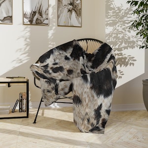 Könnte beinhalten: Eine schwarze und weiße Kuhfelldecke, die über einen Korbstuhl gelegt ist. Die Decke hat eine weiche, flauschige Textur und ist perfekt, um jedem Raum einen Hauch von rustikalem Charme zu verleihen.