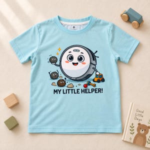 Könnte beinhalten: Ein hellblaues T-Shirt mit kurzen Ärmeln und einer Cartoon-Grafik eines lächelnden Saugroboters, umgeben von kleinen flauschigen Staubmäusen, einem Spielzeugauto und einer Hantel. Der Text "MY LITTLE HELPER!" ist darunter in Schwarz gedruckt.