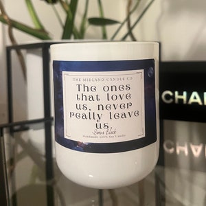 Può includere: Una candela bianca con un'etichetta blu con la scritta "The ones that love us, never really leave us." La candela è di The Midland Candle Co. ed è una candela artigianale 100% alla soia.