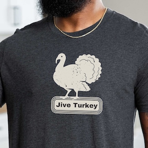 Puede incluir: Una camiseta gris oscuro con una ilustración vintage de un pavo con el texto "Jive Turkey" en un rectángulo blanco.