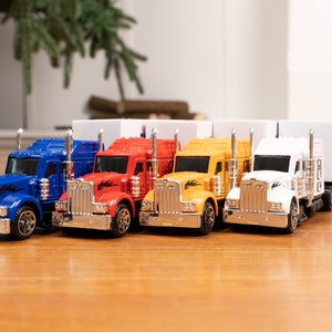 May include: Four toy semi-trucks in blue, red, yellow, and white with trailers. The trucks have silver accents and black flames on the sides.