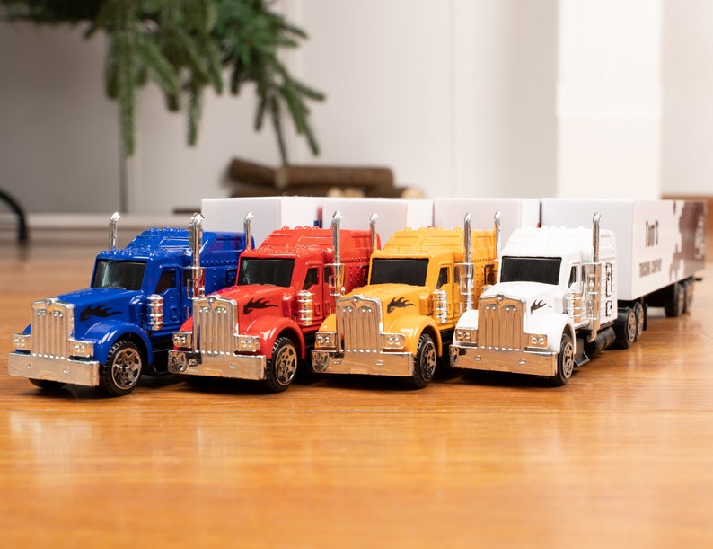 May include: Four toy semi-trucks in blue, red, yellow, and white with trailers. The trucks have silver accents and black flames on the sides.