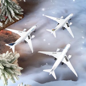May include: Three white toy airplanes with the names "David", "Arthur", and "Stuart" printed on them. The airplanes have black wheels and the word "Airliner" printed on the wings. The background has a winter theme with a Christmas tree.