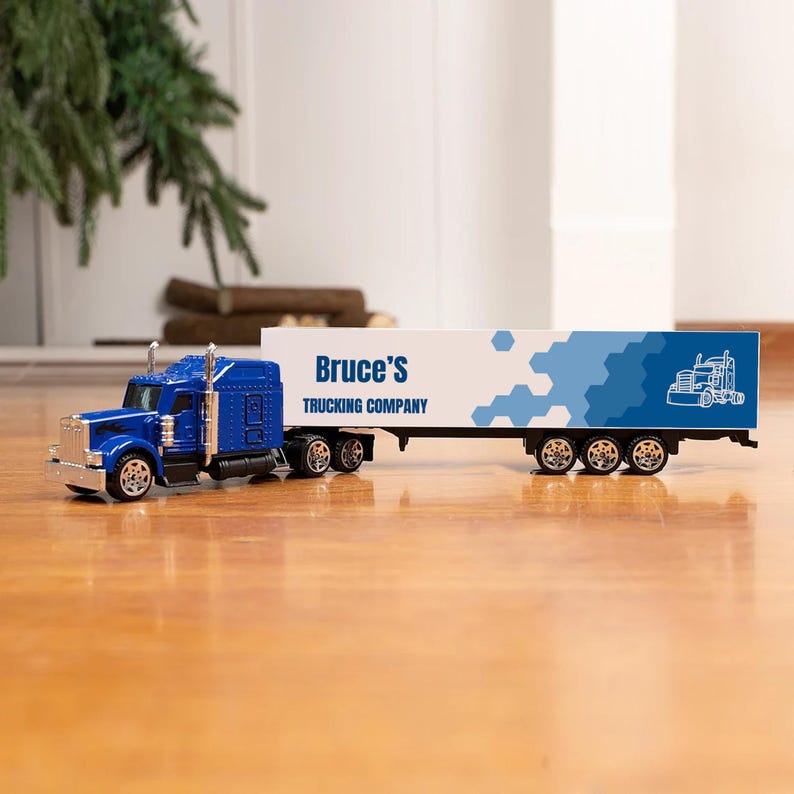 May include: Blue toy semi-truck with a white trailer. The trailer has a blue and white geometric pattern and the text "Bruce's Trucking Company".