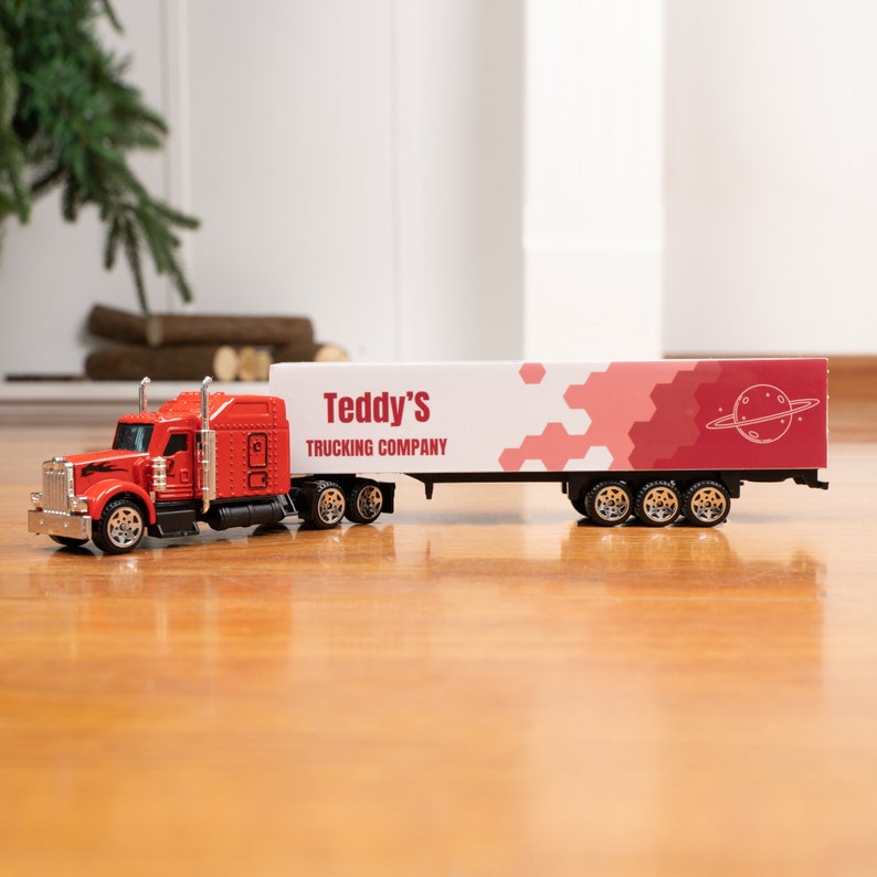 May include: Red toy semi-truck with a white trailer. The trailer has a red and white geometric design with the text "Teddy's Trucking Company".