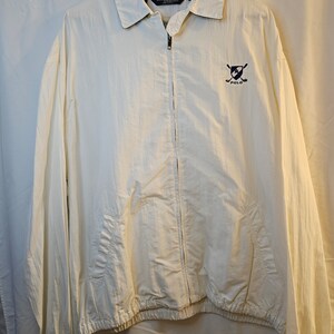 May include: A white zip-up jacket with a navy blue Polo logo featuring crossed golf clubs. The jacket has a drawstring at the bottom and elastic cuffs.
