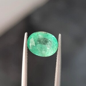 May include: A vibrant green oval emerald gemstone, held in a pair of tweezers.
