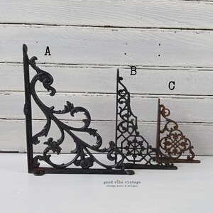 May include: Three decorative cast iron shelf brackets in varying styles. The brackets are in black and brown tones. The brackets are labeled A, B, and C. The brackets are in a vintage style.