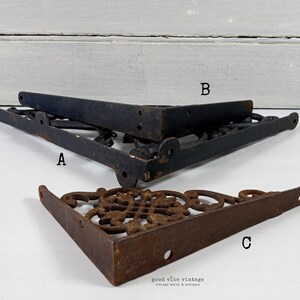 May include: Three vintage cast iron shelf brackets. Two are black, and one is a rusty brown color. The brackets are in a corner shape with decorative scrollwork. The brackets are labeled A, B, and C.