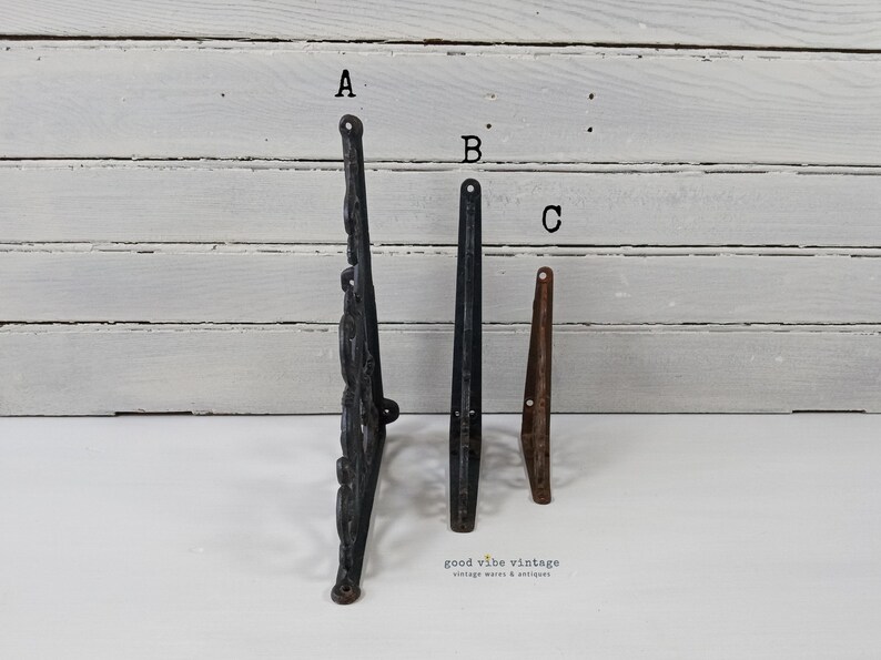 May include: Three vintage metal furniture legs are displayed against a white background. The legs are in different styles and colors: a black ornate leg, a black straight leg, and a brown tapered leg. The shop's name, "good vibe vintage", is at the bottom.