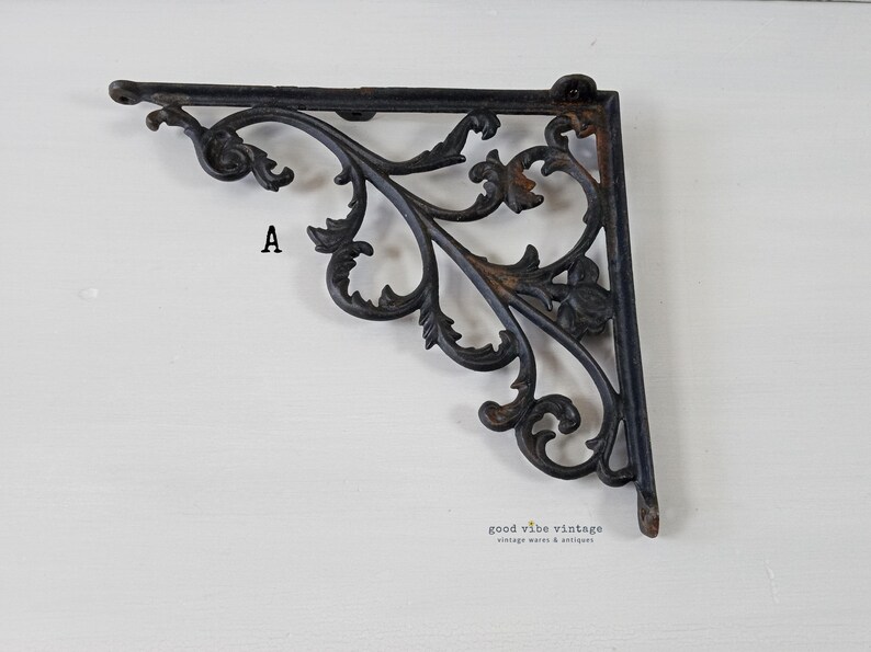 May include: Ornate black metal shelf bracket with a scrolling leaf design. The bracket is in an L-shape and features the letter "A". The bracket is a vintage item.