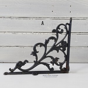 May include: Black, ornate cast iron shelf bracket with a decorative floral and scroll design. The bracket is in the shape of an L, with mounting holes for easy installation. The bracket is a vintage item.