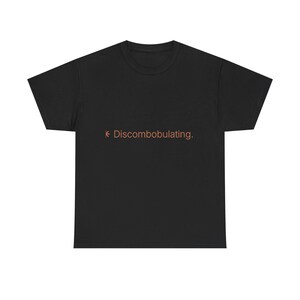 May include: A black short-sleeved t-shirt featuring the word Discombobulating. printed in a light brown colour across the centre of the chest. The text is accompanied by a small, simple star-like graphic symbol positioned to the left of the word.