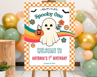 May include: A Halloween-themed sign with a cartoon ghost holding a pumpkin and flower. The sign reads "Spooky One" and "Welcome to Antonia's 1st Birthday" with a retro rainbow design and orange checkered border. Balloons in gold, white, and green surround the sign.