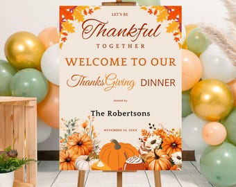 May include: A Thanksgiving dinner welcome sign on an easel, featuring the text "Let's Be Thankful Together" and "Welcome to Our Thanksgiving Dinner." The sign is decorated with fall foliage and pumpkins, with balloons in the background.