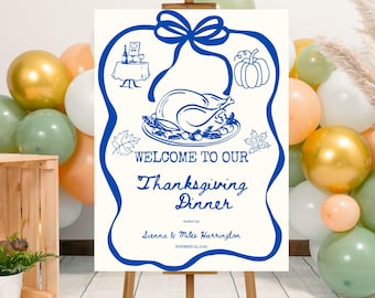 May include: Thanksgiving dinner welcome sign on an easel. The sign is cream-colored with a blue border and illustrations of a turkey, pumpkin, and table setting. Text reads "Welcome to our Thanksgiving Dinner" and includes names and a date.