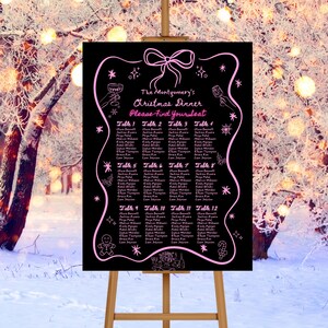May include: A black seating plan on an easel, decorated with pink illustrations for a Christmas dinner. The text reads "The Montgomery's Christmas Dinner, Please Find Your Seat." Names are listed under tables 1-12.