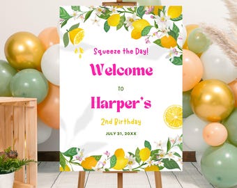 May include: A welcome sign on an easel with the text "Squeeze the Day! Welcome to Harper's 2nd Birthday July 31, 20XX." The sign is decorated with lemons and flowers. Balloons in gold, white, peach, and green surround the sign.