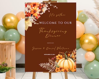 May include: A Thanksgiving dinner welcome sign on a wooden easel. The sign is brown with floral and pumpkin illustrations. Text reads "Welcome to Our Thanksgiving Dinner" and includes the hosts' names and date. Balloons in gold, white, and green are in the background.