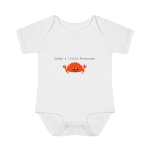 Könnte beinhalten: Weißer Baby-Strampler mit kurzen Ärmeln, auf dem ein roter Cartoon-Krebs mit dem Text "Daddy's little Crustacean" aufgedruckt ist.