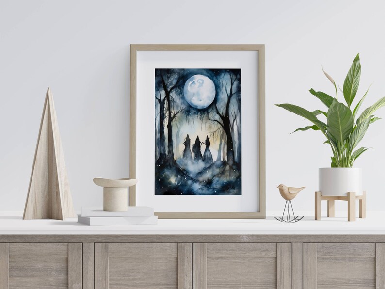 May include: A watercolor painting of three figures in a forest under a full moon. The figures are silhouetted against the moon and the trees. The painting is framed in a light wood frame.