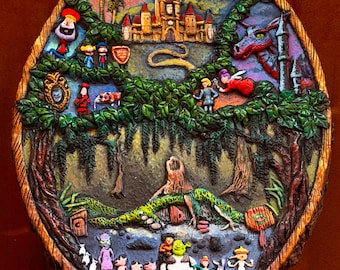 May include: A circular wooden plaque featuring a relief sculpture of a fantasy scene with a castle, a dragon, and various characters including an ogre, a donkey, and small pigs. The artwork is painted in vibrant colors with green foliage.