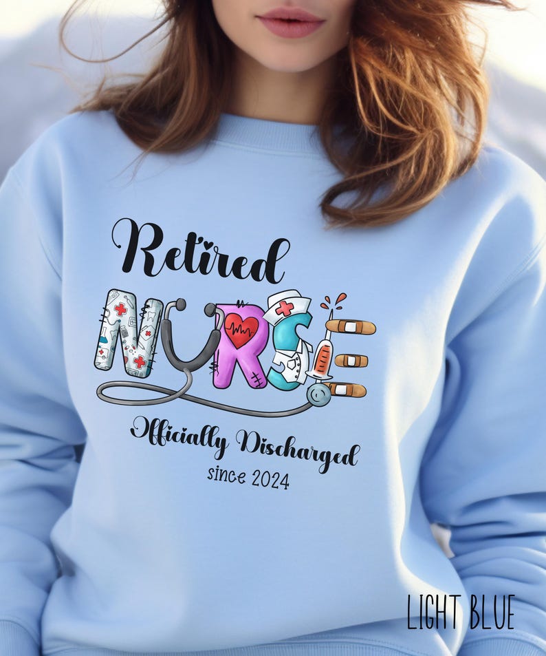 May include: Light blue sweatshirt with the text "Retired Nurse Officially Discharged since 2024" and a colorful graphic of a stethoscope and medical symbols.