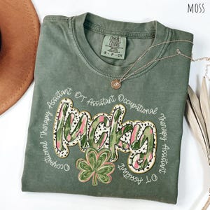 May include: Green t-shirt with a white graphic that says "Occupational Therapy Assistant OT Assistant Occupational Therapy Assistant OT Assistant" with a shamrock and the word "Lucky" in a green, pink, and white patterned font.
