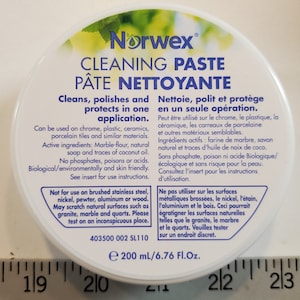 May include: A white round container with a blue Norwex logo and the text "Cleaning Paste" and "Pâte Nettoyante". The container is labeled with instructions for use and cautions about surfaces not to use the paste on. The container is 200 ml or 6.76 fluid ounces.