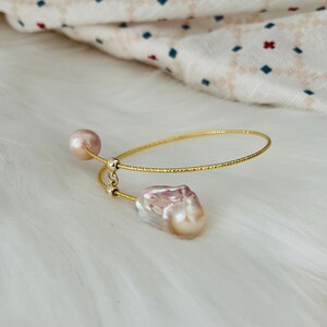 Peut inclure: Un bracelet jonc en or avec deux perles baroques roses. Le bracelet est fait de fil d'or fin et textur&eacute;.