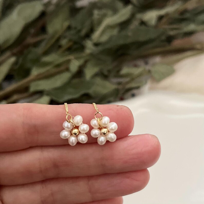 May include: A pair of gold dangle earrings with small white pearl flowers. Each flower has six pearls and a gold bead in the center.