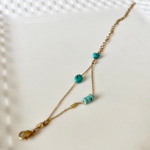 May include: A delicate gold chain bracelet with turquoise and blue beads. The bracelet has a lobster clasp closure.