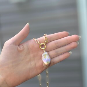 以下が含まれることがあります： 大きな虹色のバロックパールペンダントが付いたゴールドトーンのネックレス。 ネックレスは長方形のリンクと円形の留め金が付いたチェーンです。 パールはピンク、ゴールド、グリーンなど、さまざまな色を表示します。