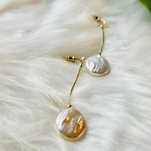 May include: A pair of gold dangle earrings with white pearl accents. The pearls are round and have a textured surface.