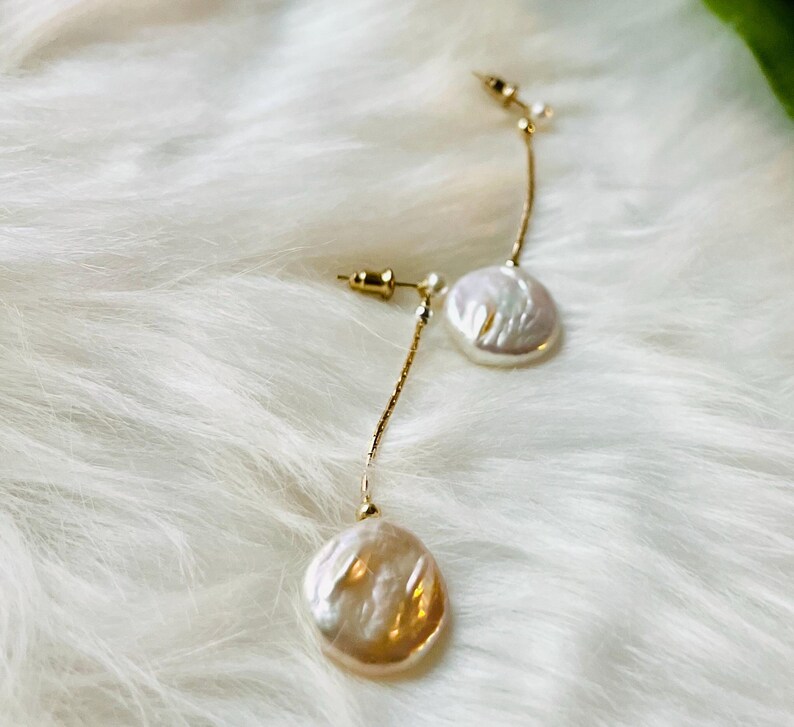 May include: A pair of gold dangle earrings with white pearl accents. The pearls are round and have a textured surface.