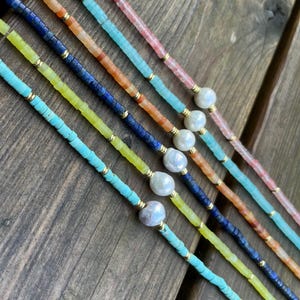 May include: Five layered necklaces with different colored beads and a pearl accent on each strand. The necklaces are made with turquoise, yellow, blue, orange, and pink beads.