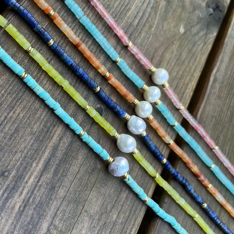 May include: Five layered necklaces with different colored beads and a pearl accent on each strand. The necklaces are made with turquoise, yellow, blue, orange, and pink beads.
