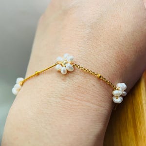 May include: A delicate gold chain bracelet with small white pearl flower accents.