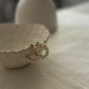 May include: A pair of gold hoop earrings with a circle of white pearls around each hoop.