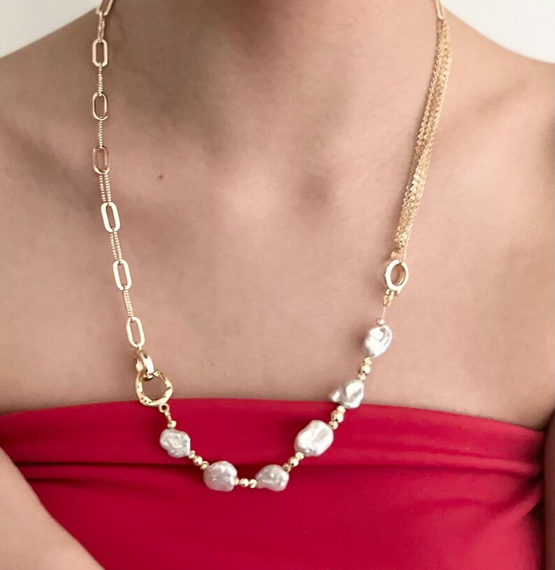 Peut inclure: Un collier dor&eacute; avec une combinaison de cha&icirc;nes et de perles blanches irr&eacute;guli&egrave;res. Le collier pr&eacute;sente un design unique, m&eacute;langeant diff&eacute;rentes textures et formes, cr&eacute;ant un bijou remarquable.