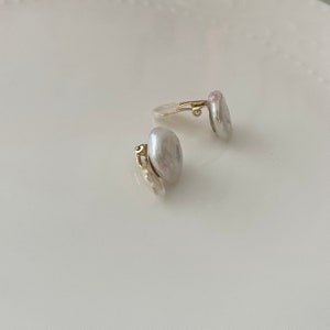 May include: A pair of pearl clip-on earrings with gold-tone clasps. The pearls are a soft white color and have an irregular shape.