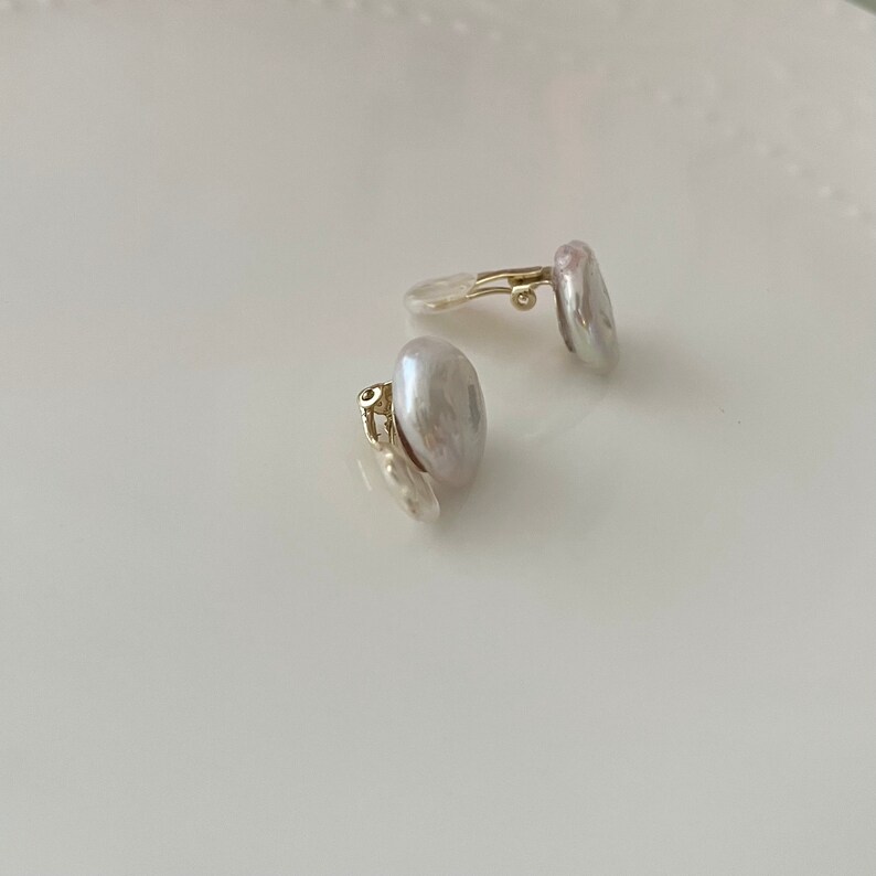May include: A pair of pearl clip-on earrings with gold-tone clasps. The pearls are a soft white color and have an irregular shape.
