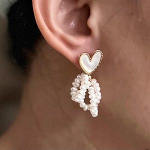 May include: Gold heart shaped earrings with a white pearl drop. The heart is made of mother of pearl.
