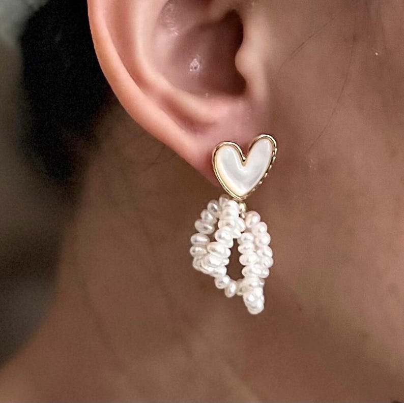 May include: Gold heart shaped earrings with a white pearl drop. The heart is made of mother of pearl.