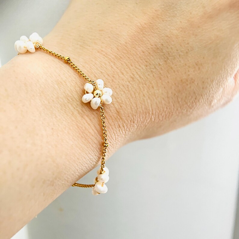 May include: A gold chain bracelet with small white pearl flower accents.