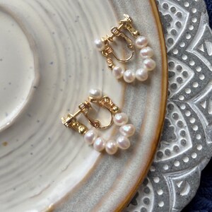 May include: A pair of gold-tone clip-on earrings with a row of white pearls around the edge of each earring.