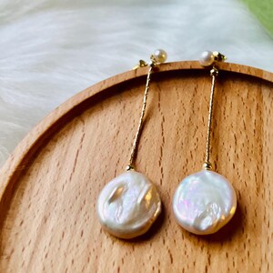 May include: A pair of gold dangle earrings with a white pearl drop. The pearls are round and have a slight iridescent sheen.